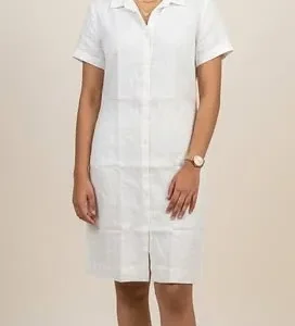 A woman wearing a white linen dress with short sleeves and buttons, smiling against a neutral background.